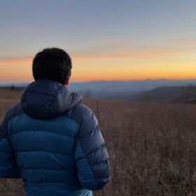 man in jacket looking out at sunset over hills