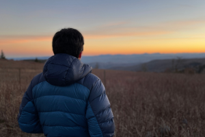 student in a jacket looking at sunset over the hills